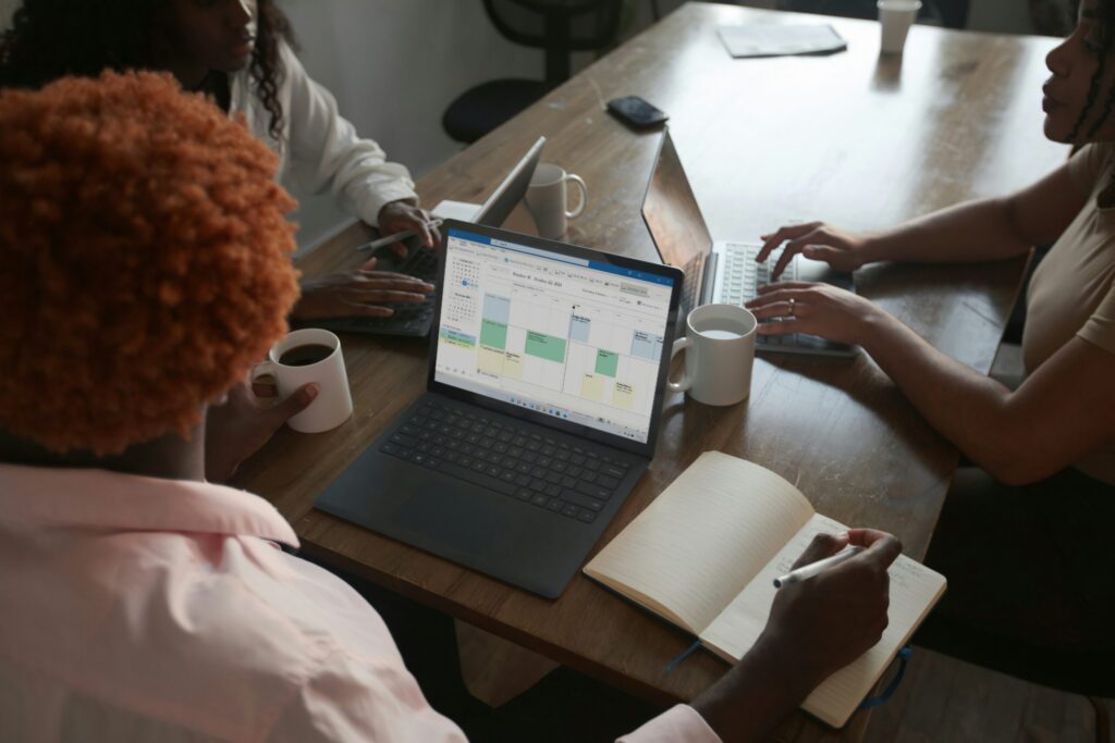 Three people in a meeting at a table discussing schedule on their Microsoft laptop